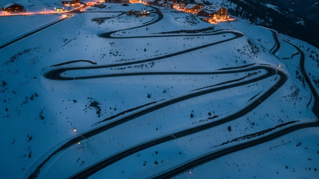 Vue aérienne d’une route de montagne en lacets dégagée dans la neige, station éclairée sur le plateau