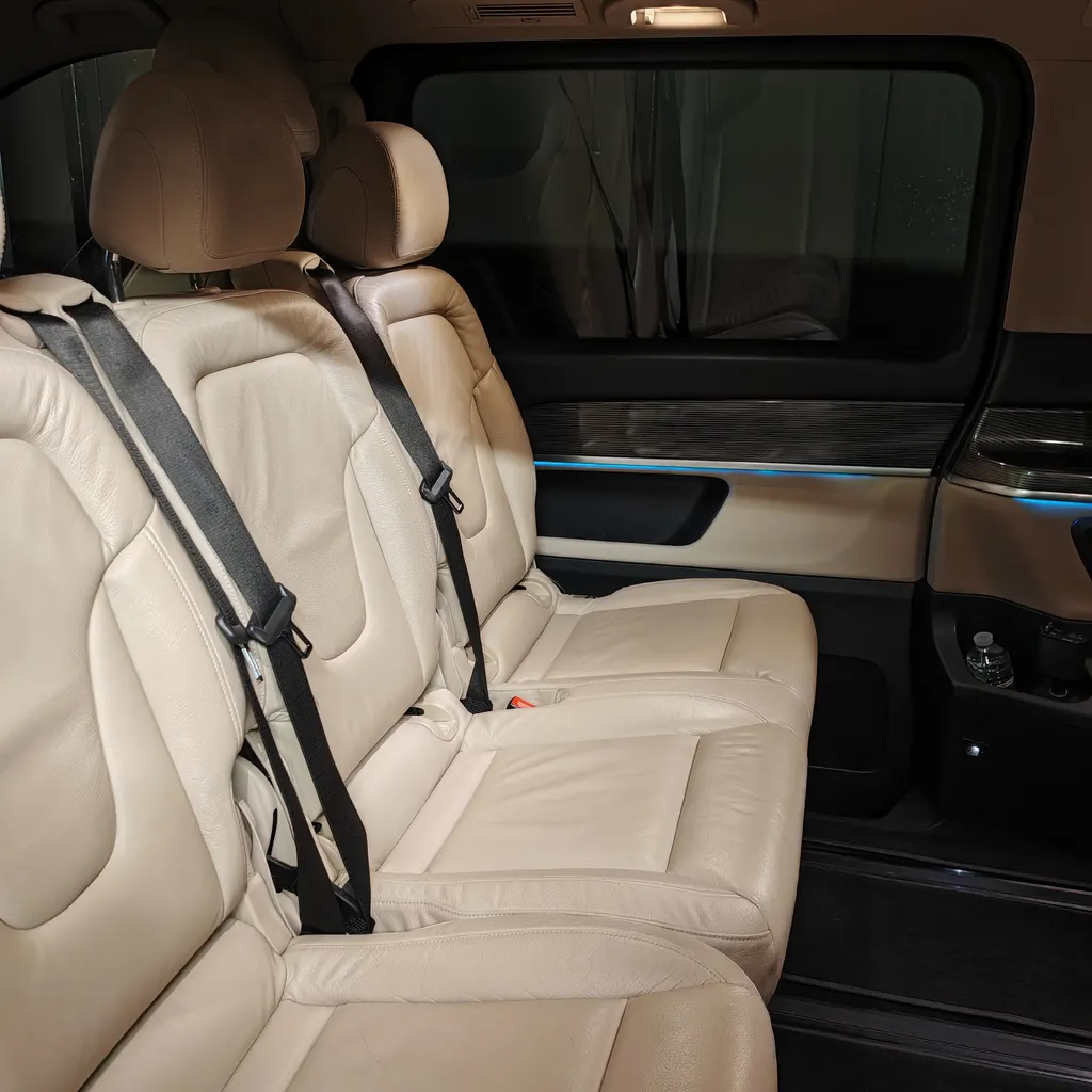Intérieur d’une Mercedes Classe V, sièges cuir beige face à la route et éclairage d’ambiance