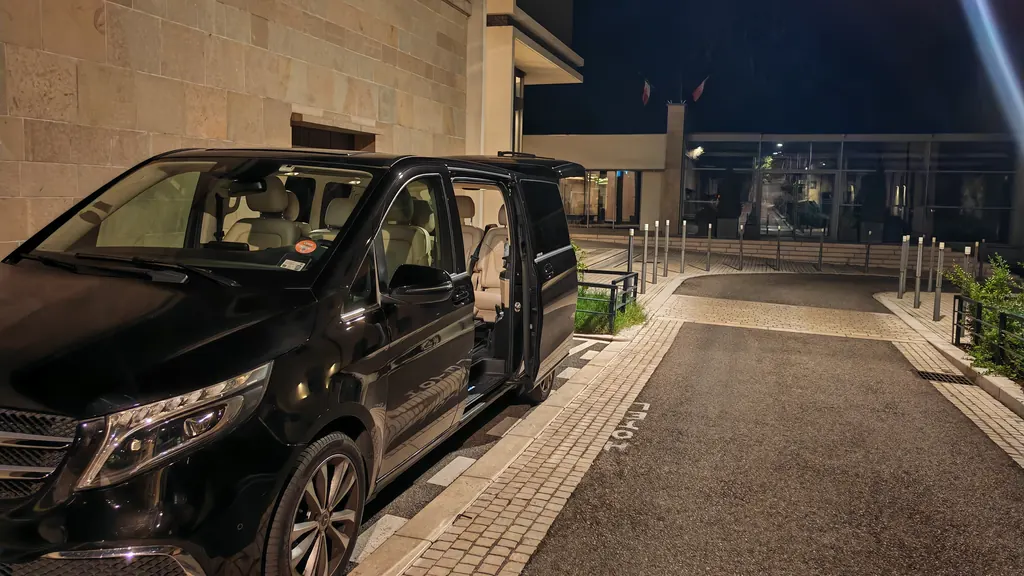 Mercedes Classe V noire portes latérales ouvertes la nuit, habitacle cuir beige éclairé, devant l’entrée d’un bâtiment