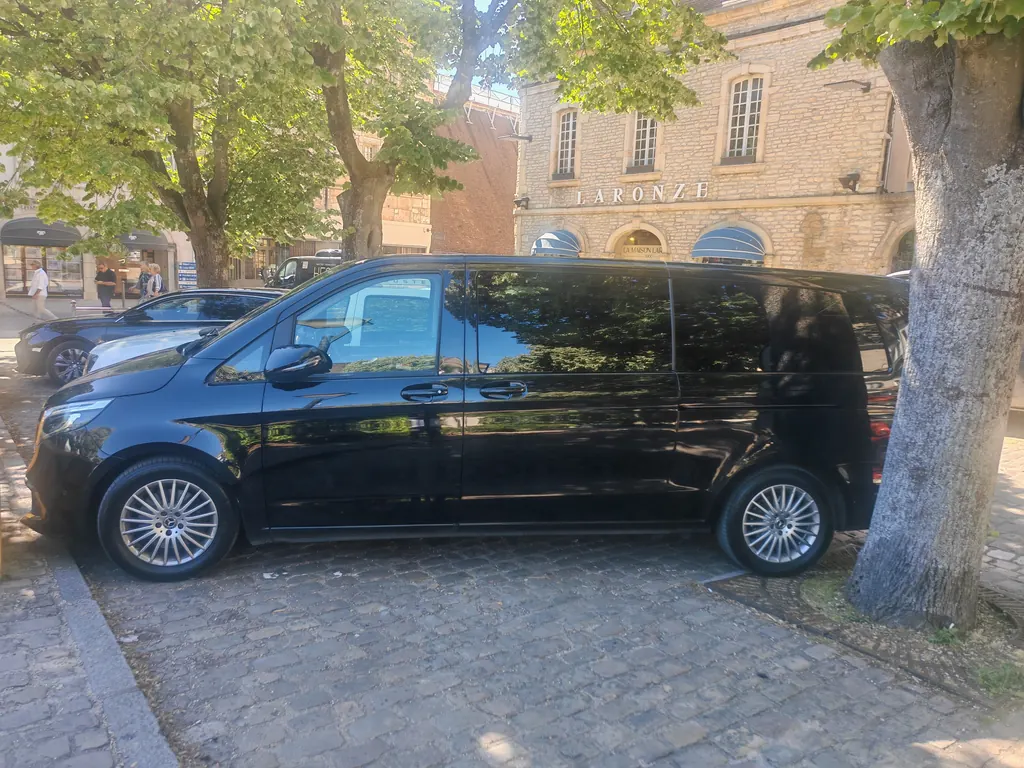 Mercedes Classe V noire de profil sous les platanes d’une place de ville